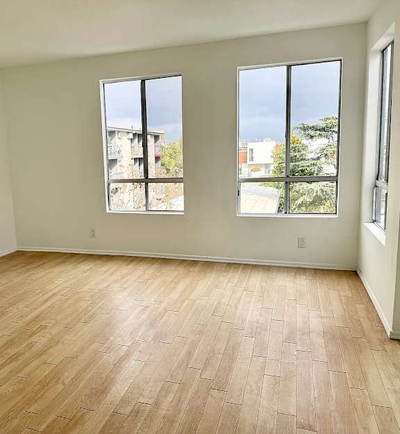A room with wooden flooring and two windows.