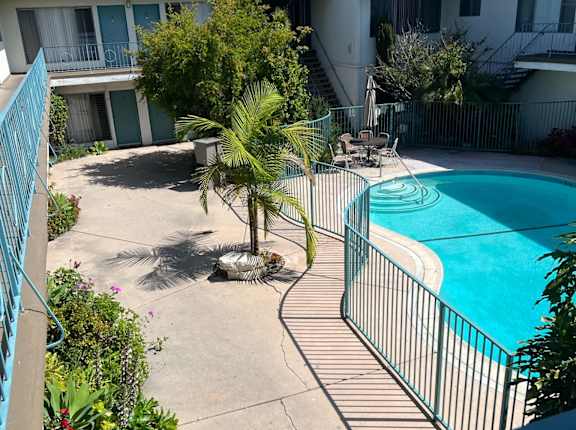 A pool surrounded by a fence and a patio with a table and chairs.