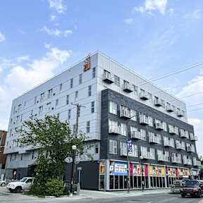 A large building with a grey facade and a red sign on the top.
