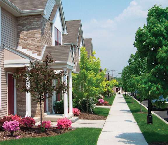 A residential street with houses on both sides and a sidewalk in the foreground.