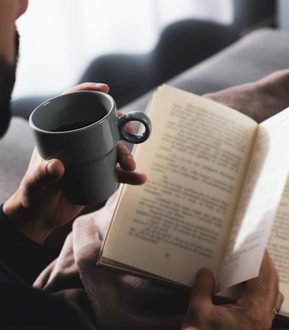Person Holding Cup of Coffee while Reading Book