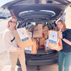 two women loading bags of food into the trunk of a car