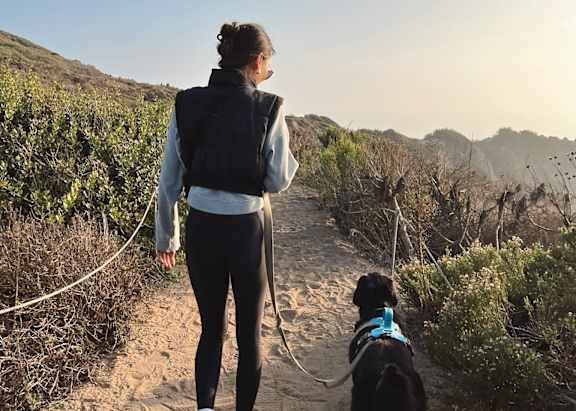 A woman and her dog are walking on a trail.