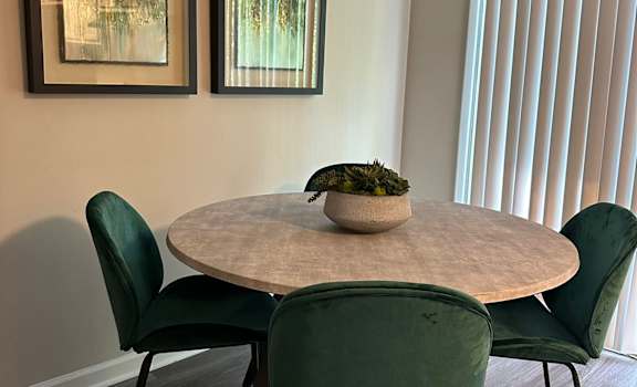 A dining table with four chairs and two pictures on the wall.