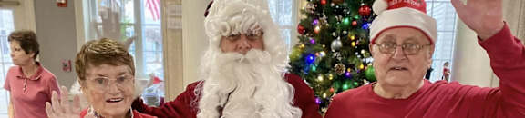 two women standing with santa claus in front of a christmas tree