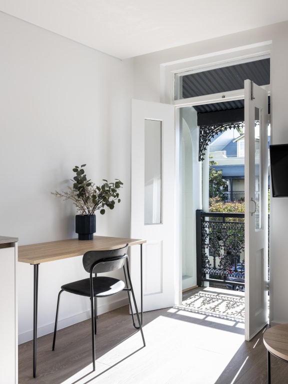 a small desk with a black chair in a room with a door and a balcony