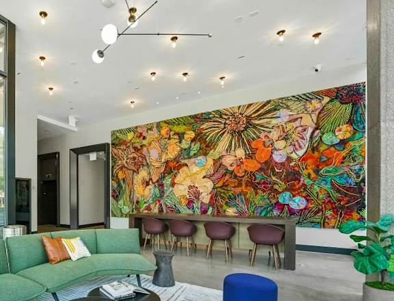 A living room with a green couch and a large mural on the wall.