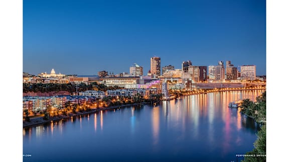 A city skyline at dusk with buildings reflecting in the water.