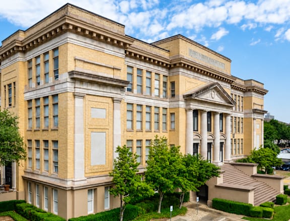 A large, beige building with a row of windows on the ground floor and a row of columns on the upper floor.