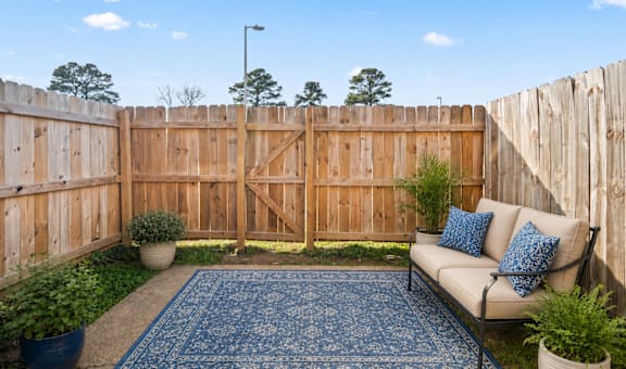 A blue rug sits on a wooden deck with a white couch and potted plants.