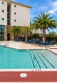 A swimming pool in front of a building with palm trees.