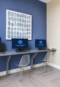 Three computers are on a desk with chairs.