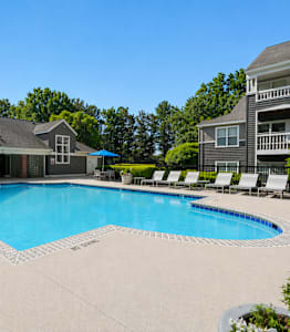 A large swimming pool in front of a house with a deck and lounge chairs.