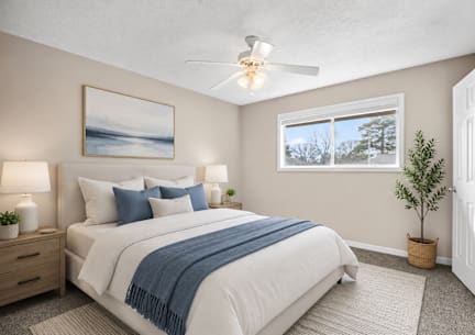 A bedroom with a bed, two lamps, a ceiling fan, and a painting on the wall.