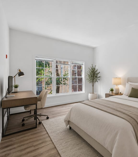 A bedroom with a large bed, a desk, and a window with a view of trees.