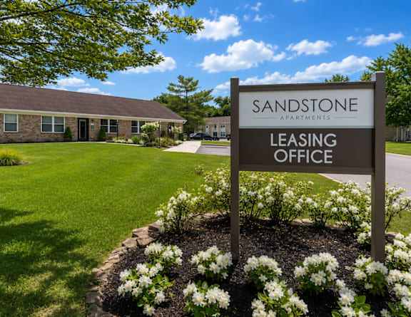 A sign for the Sandstone Apartments leasing office stands in front of a building.