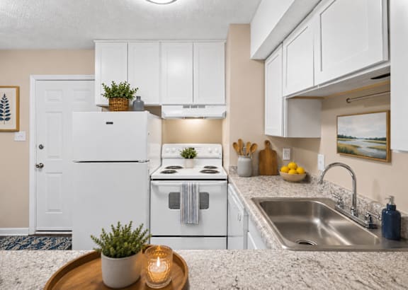 A kitchen with white appliances and a wooden tray with a plant and candle on the counter.