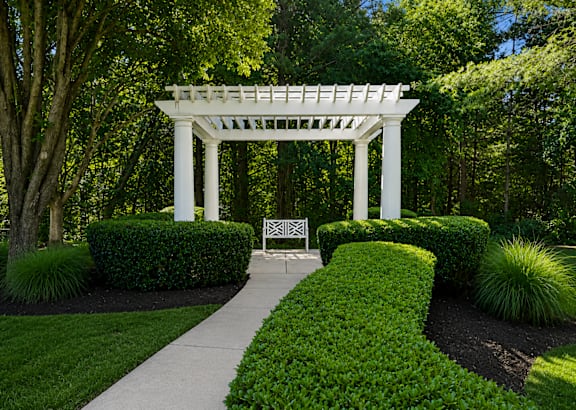 A white pergola is situated in the middle of a garden with a sign in front of it.