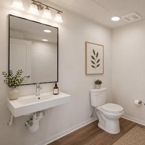 A white bathroom in a studio unit with a toilet, sink, and mirror.