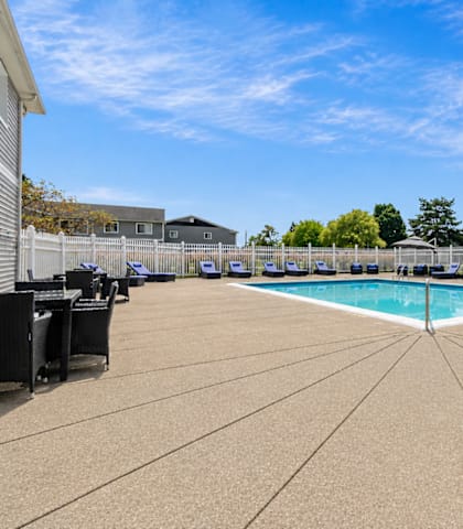 A large outdoor swimming pool surrounded by a concrete patio and a white fence.