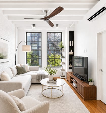 A living room with a white couch, a television, and a plant.