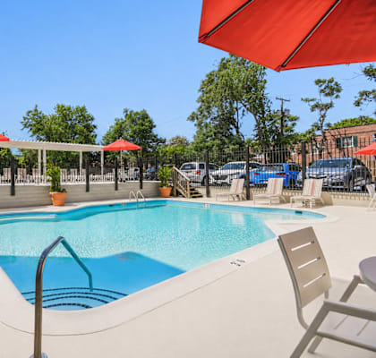 A large outdoor swimming pool with red umbrellas and lounge chairs.