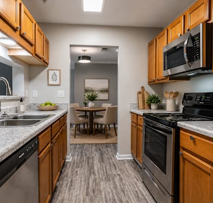 Modern apartment kitchen at Lancaster Place Apartments in Calera, Alabama with stainless-steel appliances, wood cabinetry, generous counter space, and ample storage.