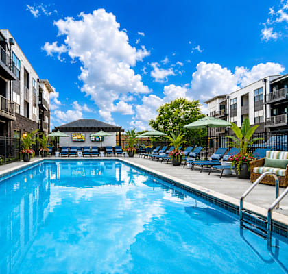 A swimming pool in a residential area surrounded by potted plants and chairs.