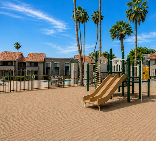 A playground with a slide, palm trees, and a swimming pool in the background.