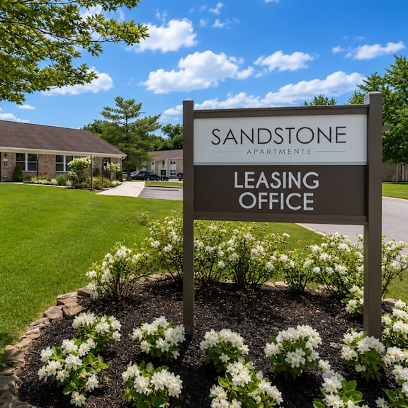 A sign for the Sandstone Apartments leasing office stands in front of a building.