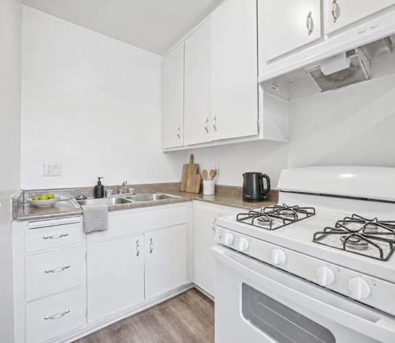 A white kitchen with a stove top oven and a sink.