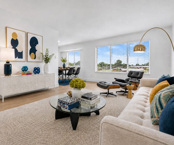 A living room with a white couch, a coffee table, and a large window with a view of the outside.