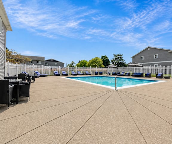 A large outdoor swimming pool surrounded by a concrete patio and a white fence.
