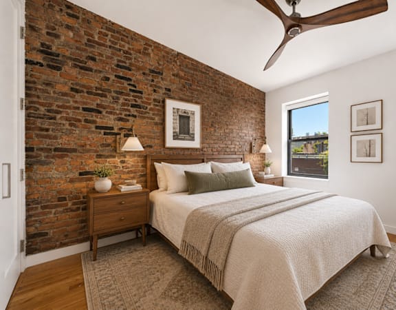 A bedroom with a brick wall and a bed with a white comforter.