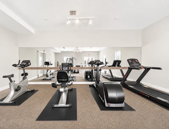 A gym with a row of treadmills, elliptical machines, and stationary bikes.