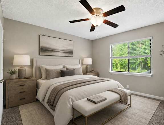 A bedroom with a large bed, a ceiling fan, and a window showing greenery outside.