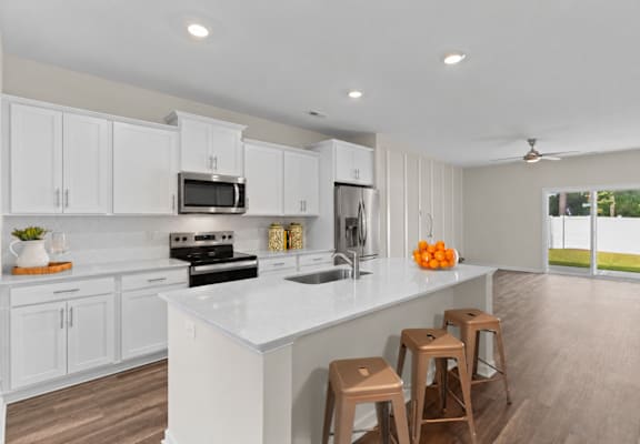 A kitchen with white cabinets and a white island with three stools.