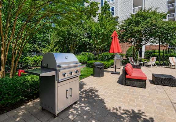 A BBQ grill is in the middle of a patio surrounded by furniture.