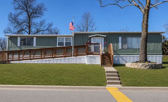 A green house with a flag on the roof and a tree in front.