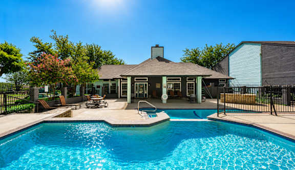 A pool in front of a house with a sunny sky.