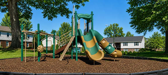 A playground with a green slide and brown sandbox.