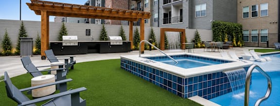 A pool with a slide and a pergola in the foreground with apartment buildings in the background.