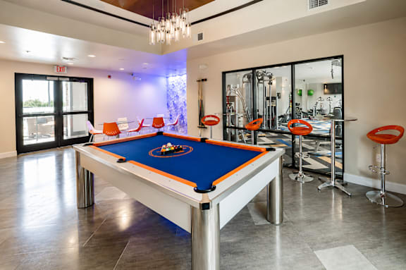 A pool table is in the middle of a room with a bar area.