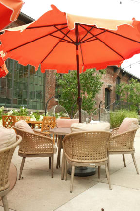 a patio with tables and chairs under an orange umbrella