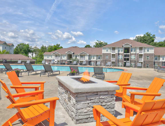 A fire pit sits in the middle of a patio with orange chairs around it.