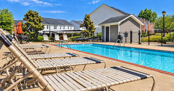 A pool with sun loungers and a building in the background.