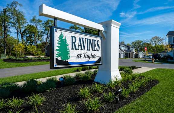 A sign for Ravines at Taylor is displayed in front of a residential area.