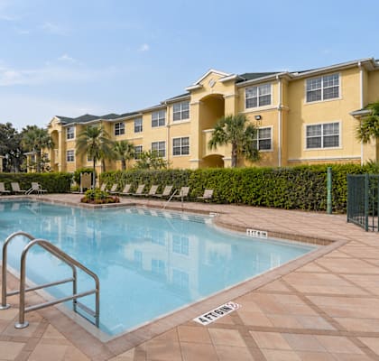 A pool surrounded by a tiled patio and a building in the background.