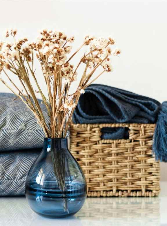 a stack of blankets and a blue vase with flowers on a table