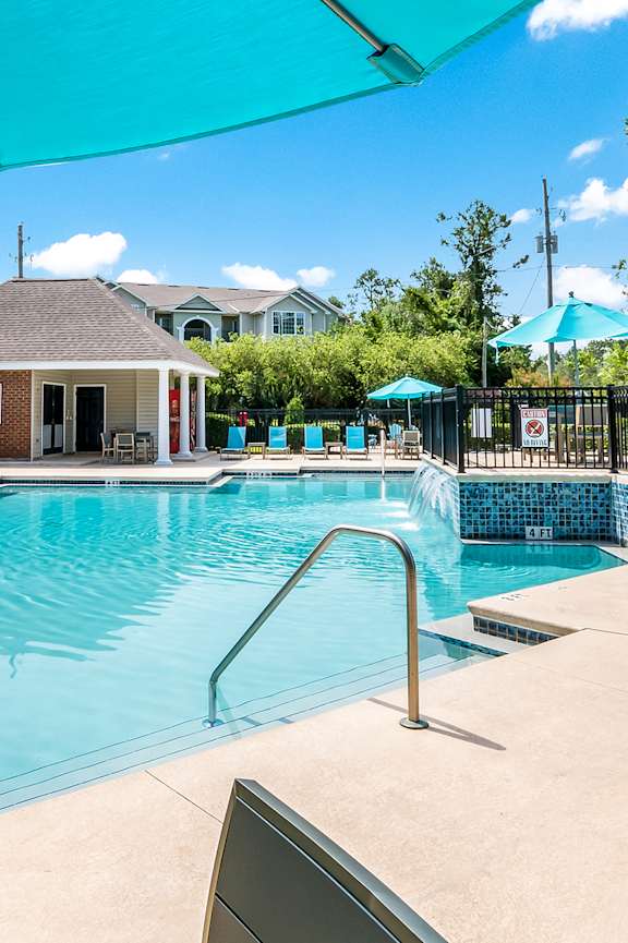 A large swimming pool with a blue umbrella and lounge chairs.